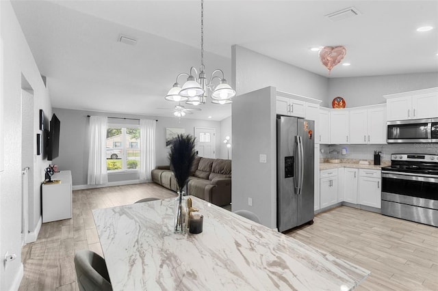 122 Seville Rd, Auburndale, FL 33823 - kitchen with appliances with stainless steel finishes, open floor plan, white cabinetry, light wood-style flooring, and light stone counters