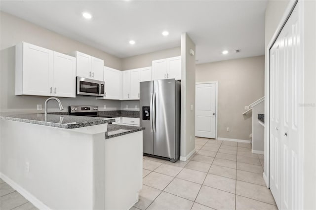11632 Castine St, New Port Richey, FL 34654 - kitchen featuring appliances with stainless steel finishes, a peninsula, dark stone countertops, white cabinets, and light tile patterned flooring