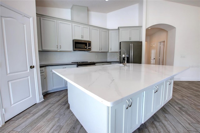 1727 Butterfly Way, Longwood, FL 32750 - kitchen with stainless steel appliances, arched walkways, light wood-style floors, a sink, and a center island with sink