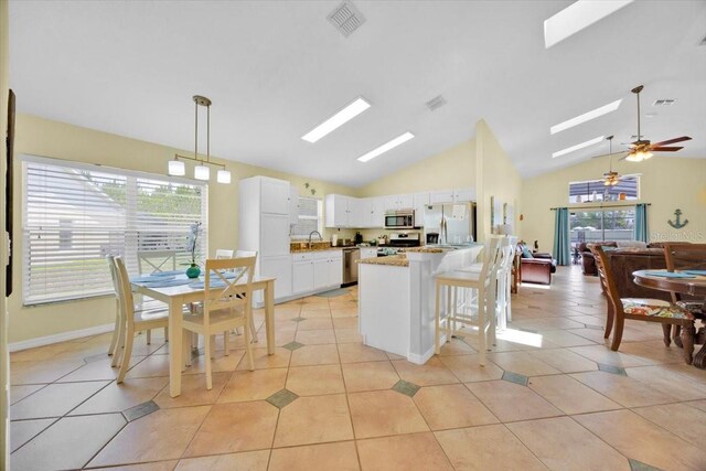2627 Autumn Creek Cir, Kissimmee, FL 34747 - kitchen featuring stainless steel appliances, a skylight, vaulted ceiling, white cabinetry, and decorative light fixtures