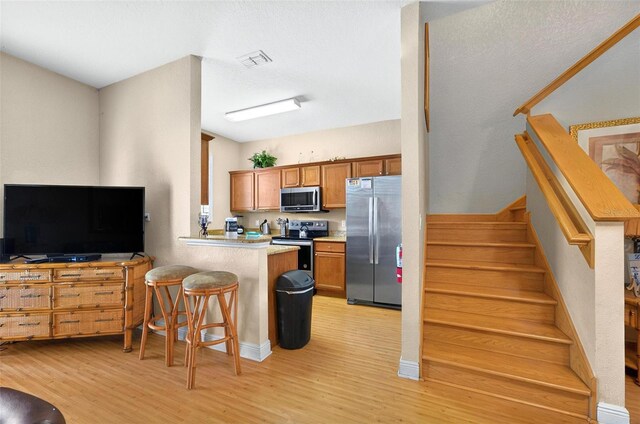 3725 Calabria Ave, Davenport, FL 33897 - kitchen with stainless steel appliances, light wood finished floors, a breakfast bar area, a peninsula, and brown cabinetry