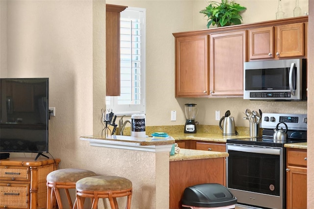 3725 Calabria Ave, Davenport, FL 33897 - kitchen featuring stainless steel appliances, brown cabinetry, a breakfast bar area, a textured wall, and a peninsula