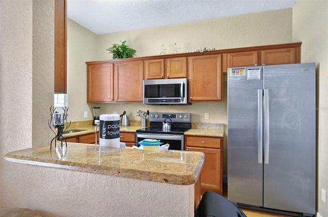 3725 Calabria Ave, Davenport, FL 33897 - kitchen with stainless steel appliances, a peninsula, brown cabinets, a textured wall, and light stone counters