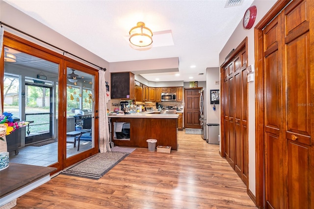 493 Princewood Dr, Deland, FL 32724 - kitchen with stainless steel appliances, light wood-style floors, a peninsula, brown cabinetry, and light countertops