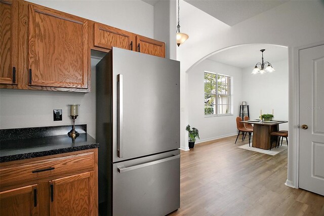 2306 Valhalla Dr, Tavares, FL 32778 - kitchen with freestanding refrigerator, arched walkways, brown cabinetry, dark countertops, and wood finished floors