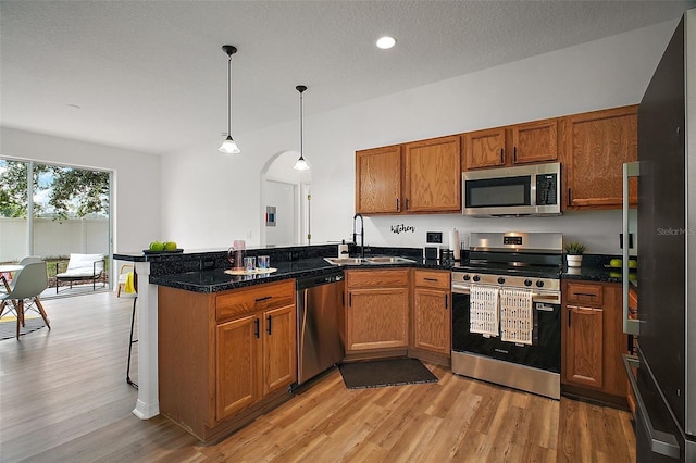 2306 Valhalla Dr, Tavares, FL 32778 - kitchen with stainless steel appliances, a sink, brown cabinets, light wood finished floors, and a peninsula