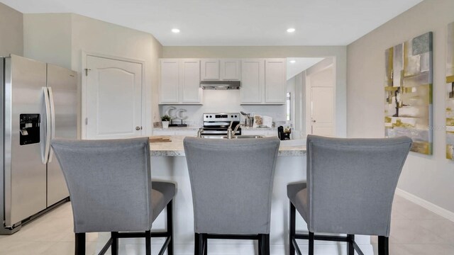 946 Princess Sabal Pt, Haines City, FL 33844 - kitchen with appliances with stainless steel finishes, under cabinet range hood, light countertops, a sink, and a breakfast bar area