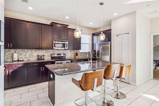 4740 Sleepy Hollow Dr, Kissimmee, FL 34746 - kitchen featuring appliances with stainless steel finishes, a sink, light marble finish floors, a breakfast bar, and dark stone counters