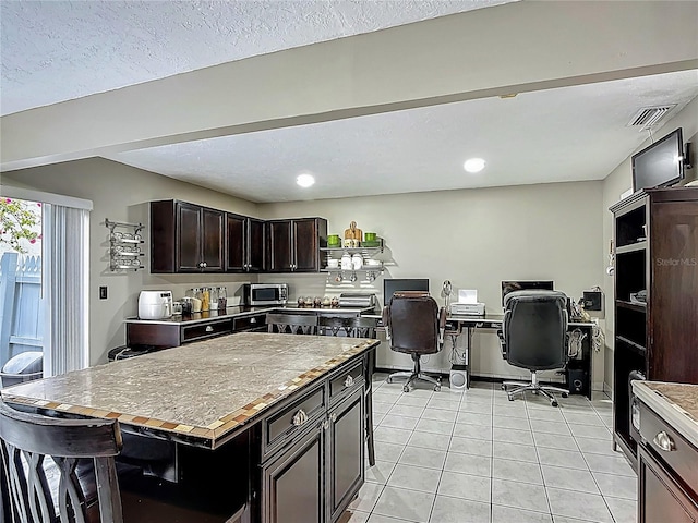 620 Wood Dr, Kissimmee, FL 34759 - kitchen with stainless steel microwave, an office area, a kitchen island, light tile patterned floors, and dark brown cabinetry