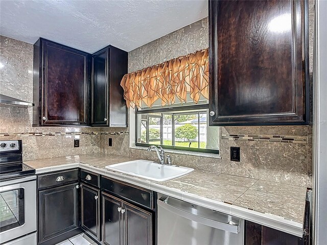 620 Wood Dr, Kissimmee, FL 34759 - kitchen with appliances with stainless steel finishes, a sink, tasteful backsplash, tile counters, and a textured ceiling