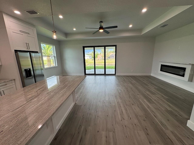 9 Bunker Pl, Rotonda West, FL 33947 - unfurnished living room featuring a raised ceiling, dark wood-style flooring, a glass covered fireplace, baseboards, and ceiling fan