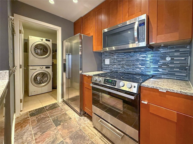 3034 Parkway Blvd Unit 102, Kissimmee, FL 34747 - kitchen with appliances with stainless steel finishes, stacked washing machine and dryer, brown cabinetry, backsplash, and light stone countertops