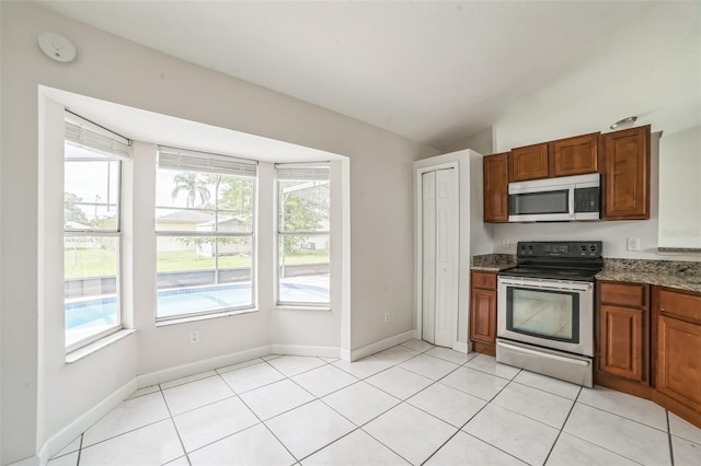 657 Mckinley Ct, Kissimmee, FL 34758 - kitchen featuring stainless steel appliances, plenty of natural light, vaulted ceiling, brown cabinets, and stone countertops