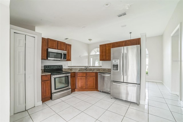 657 Mckinley Ct, Kissimmee, FL 34758 - kitchen featuring stainless steel appliances, a sink, light tile patterned floors, and brown cabinetry