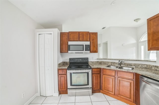 657 Mckinley Ct, Kissimmee, FL 34758 - kitchen featuring appliances with stainless steel finishes, a sink, light stone counters, light tile patterned floors, and brown cabinetry