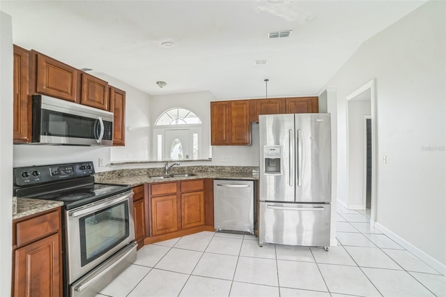 657 Mckinley Ct, Kissimmee, FL 34758 - kitchen featuring appliances with stainless steel finishes, a sink, light tile patterned floors, stone counters, and brown cabinets