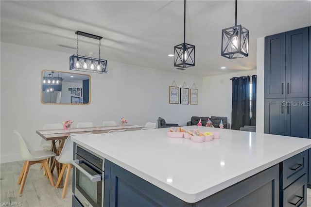 kitchen featuring light wood-type flooring, light countertops, oven, hanging light fixtures, and a center island