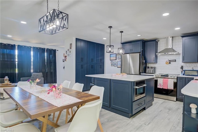 kitchen with wall chimney range hood, stainless steel appliances, light countertops, a center island, and decorative backsplash