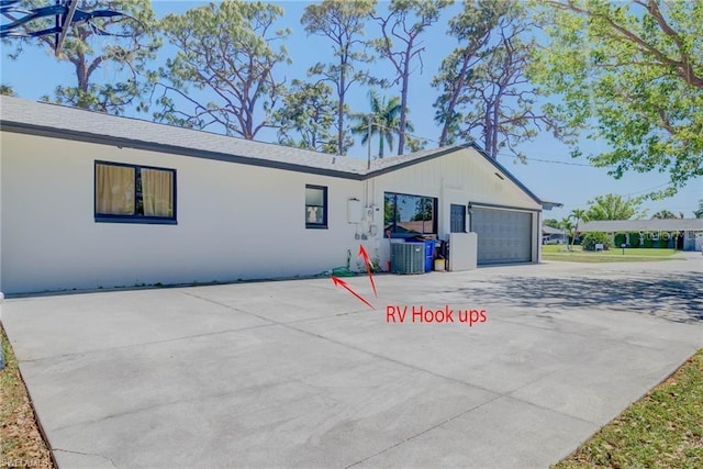 view of side of property with central AC unit, an attached garage, concrete driveway, and stucco siding