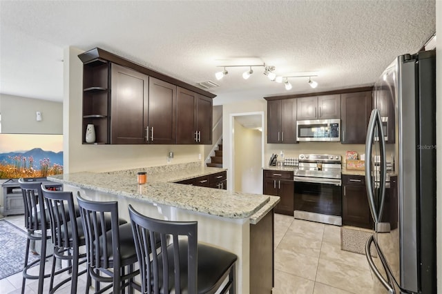 8652 Savory Dr, Orlando, FL 32825 - kitchen with stainless steel appliances, a peninsula, dark brown cabinetry, open shelves, and light tile patterned floors