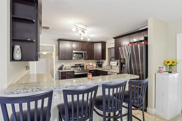 8652 Savory Dr, Orlando, FL 32825 - kitchen with stainless steel appliances, a peninsula, dark brown cabinetry, a textured ceiling, and open shelves