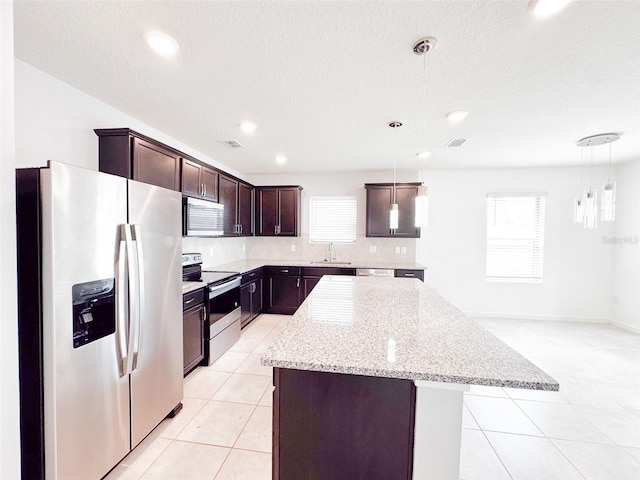398 Citrus Isle Loop, Davenport, FL 33837 - kitchen featuring appliances with stainless steel finishes, light tile patterned flooring, dark brown cabinetry, a center island, and hanging light fixtures