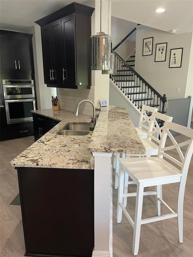 302 Coco Plum Ct, Oldsmar, FL 34677 - kitchen featuring a sink, dark cabinetry, light stone counters, backsplash, and a kitchen breakfast bar