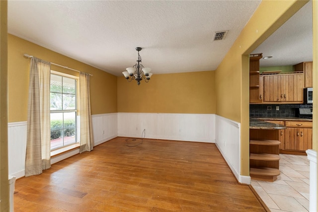16017 Johns Lake Rd, Clermont, FL 34711 - unfurnished dining area with wainscoting, light wood finished floors, a textured ceiling, and a chandelier