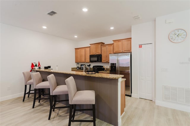 2923 Banana Palm Dr, Kissimmee, FL 34747 - kitchen with black microwave, stainless steel refrigerator with ice dispenser, a kitchen bar, light wood-type flooring, and light stone countertops