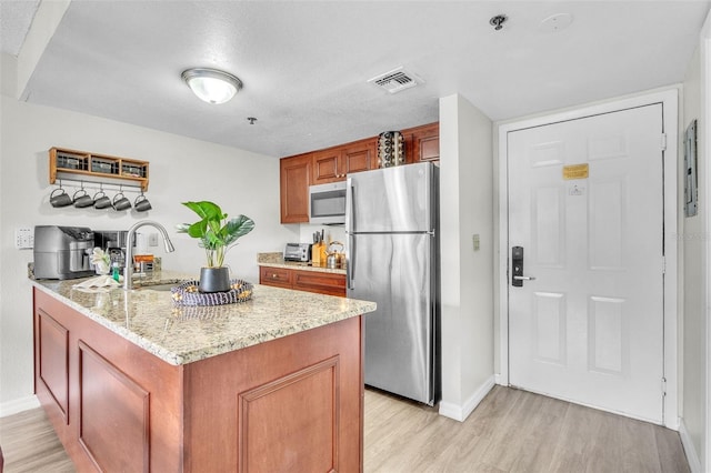 6337 Parc Corniche Dr Unit 2312, Orlando, FL 32821 - kitchen featuring appliances with stainless steel finishes, light wood finished floors, a peninsula, light stone counters, and brown cabinets