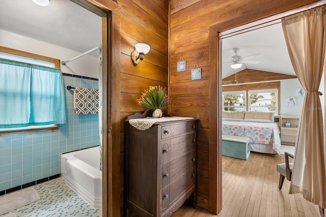 4039 S Atlantic Ave, Port Orange, FL 32127 - bathroom featuring a ceiling fan, connected bathroom, washtub / shower combination, vaulted ceiling, and wood-type flooring