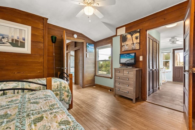 4039 S Atlantic Ave, Port Orange, FL 32127 - bedroom featuring wood walls, multiple windows, vaulted ceiling, light wood-style floors, and a ceiling fan