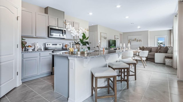 4920 Kaia Ave, Winter Haven, FL 33884 - kitchen with stainless steel appliances, light stone counters, a breakfast bar area, an island with sink, and light tile patterned flooring