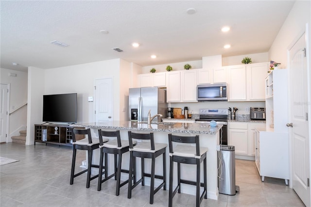 13452 Sagestone Dr, Winter Garden, FL 34787 - kitchen featuring appliances with stainless steel finishes, a kitchen island with sink, light stone counters, a kitchen bar, and recessed lighting
