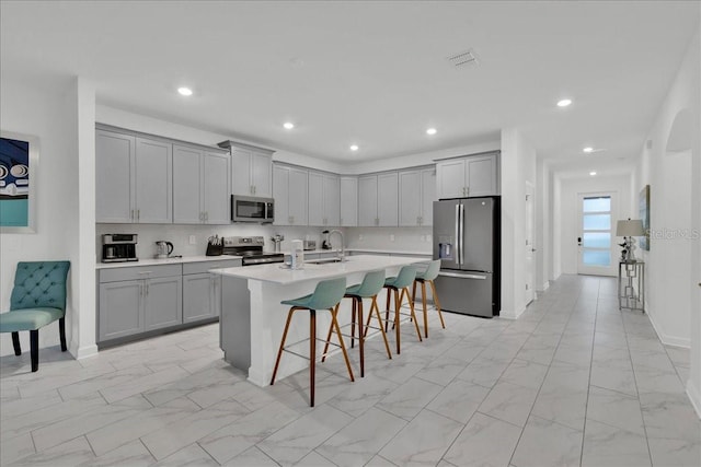 9239 Sommerset Hills Dr, Davenport, FL 33896 - kitchen with stainless steel appliances, gray cabinets, a kitchen bar, light marble finish floors, and light countertops