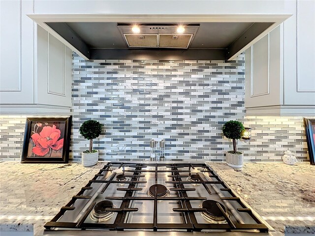 16246 Ravenna Ct, Montverde, FL 34756 - kitchen view of stainless steel gas stovetop, decorative backsplash, light stone counters, white cabinetry, and range hood