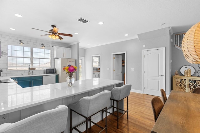 17404 Chateau Pine Way, Clermont, FL 34711 - kitchen featuring stainless steel appliances, light wood finished floors, a breakfast bar, ornamental molding, and a ceiling fan