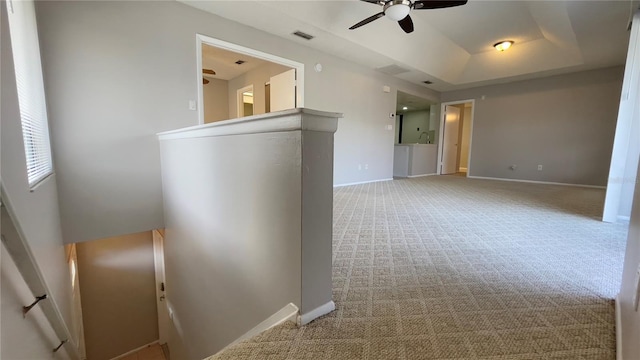 carpeted spare room featuring a ceiling fan, baseboards, and a tray ceiling