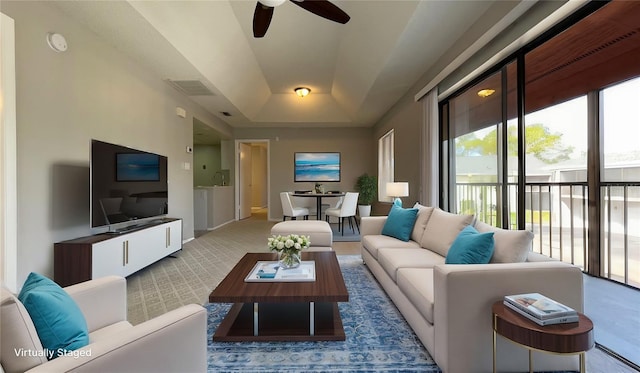 living room with a ceiling fan, a raised ceiling, carpet flooring, and baseboards