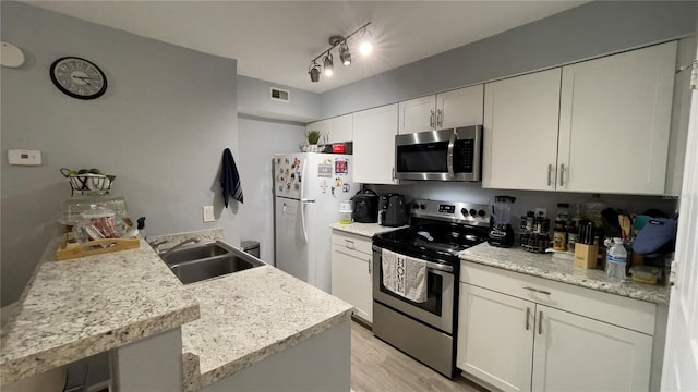 kitchen featuring stainless steel appliances, a sink, light countertops, light wood-type flooring, and white cabinetry