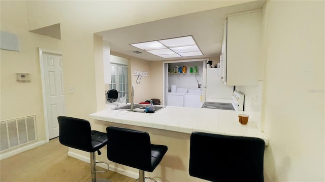 kitchen with washer and clothes dryer, a sink, tile counters, and freestanding refrigerator