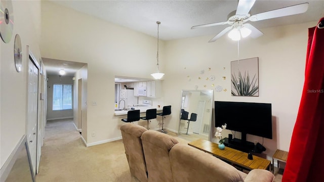 living area featuring light colored carpet, ceiling fan, baseboards, and a towering ceiling