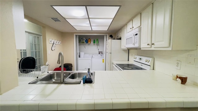 kitchen with white appliances, tile counters, washing machine and dryer, decorative backsplash, and a sink
