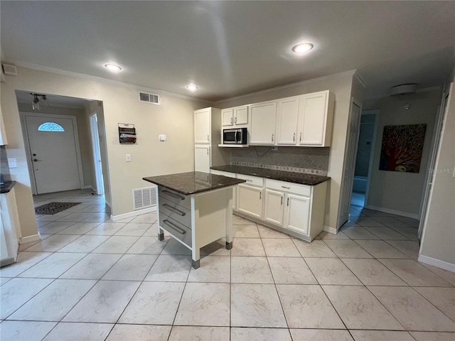7011 Archwood Dr, Orlando, FL 32819 - kitchen with stainless steel microwave, ornamental molding, white cabinetry, tasteful backsplash, and dark stone countertops