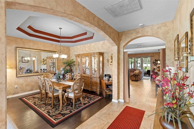 3551 Statham Dr, Apopka, FL 32712 - dining area featuring arched walkways, baseboards, a chandelier, a raised ceiling, and a textured ceiling