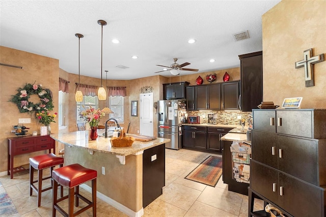 3551 Statham Dr, Apopka, FL 32712 - kitchen featuring stainless steel refrigerator with ice dispenser, a center island with sink, light stone countertops, decorative backsplash, and a ceiling fan