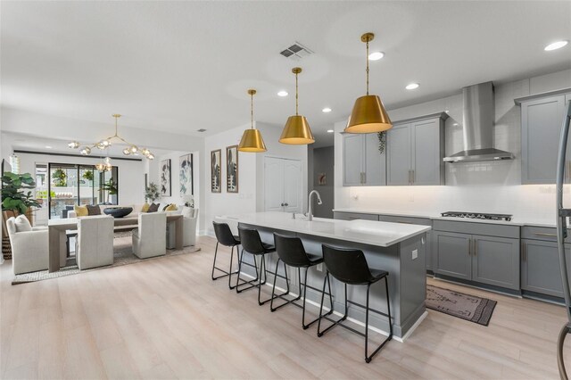 13227 Spring Grove Way, Winter Garden, FL 34787 - kitchen featuring wall chimney range hood, gray cabinetry, stainless steel gas cooktop, open floor plan, and light wood-style flooring