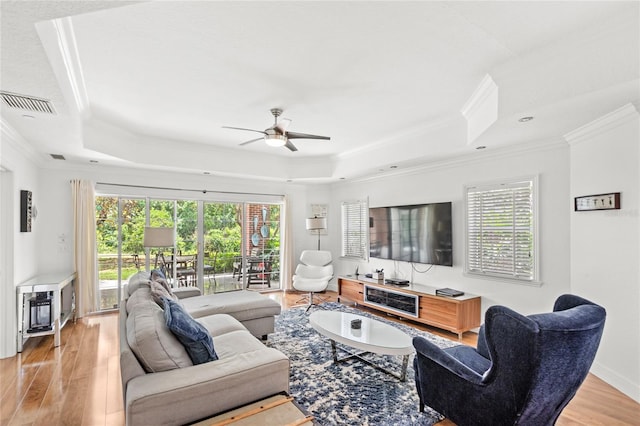 7650 Whisper Way Unit 104, Reunion, FL 34747 - living room featuring a tray ceiling, ornamental molding, a ceiling fan, light wood-style floors, and plenty of natural light