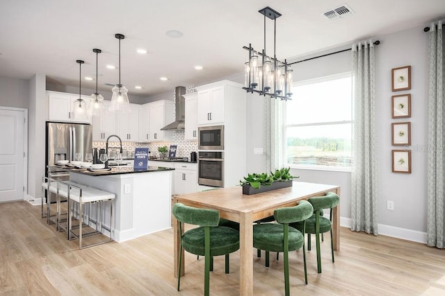 1341 Lumpini St, Saint Cloud, FL 34771 - kitchen featuring stainless steel appliances, wall chimney range hood, dark countertops, backsplash, and light wood-style flooring