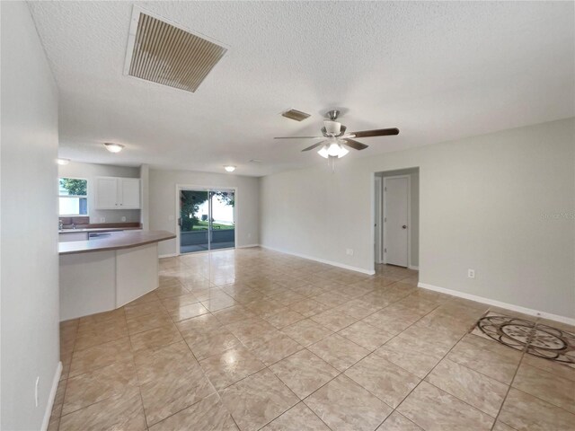 9514 SE 168th Maplesong Ln, The Villages, FL 32162 - unfurnished living room with a textured ceiling, a ceiling fan, light tile patterned flooring, a sink, and baseboards
